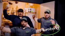 Three male plumbers posing in a service van, wearing gray shirts and caps, with a green 'Plumbing' badge overlay.