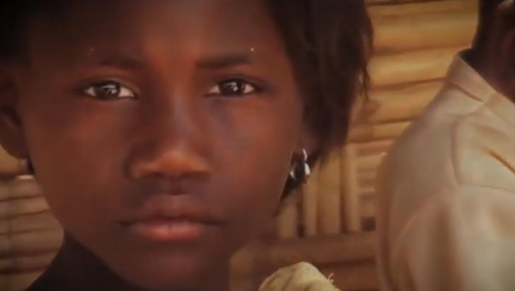 Close-up portrait of a young person with short black hair and a small hoop earring, looking at the camera against a warm wooden background