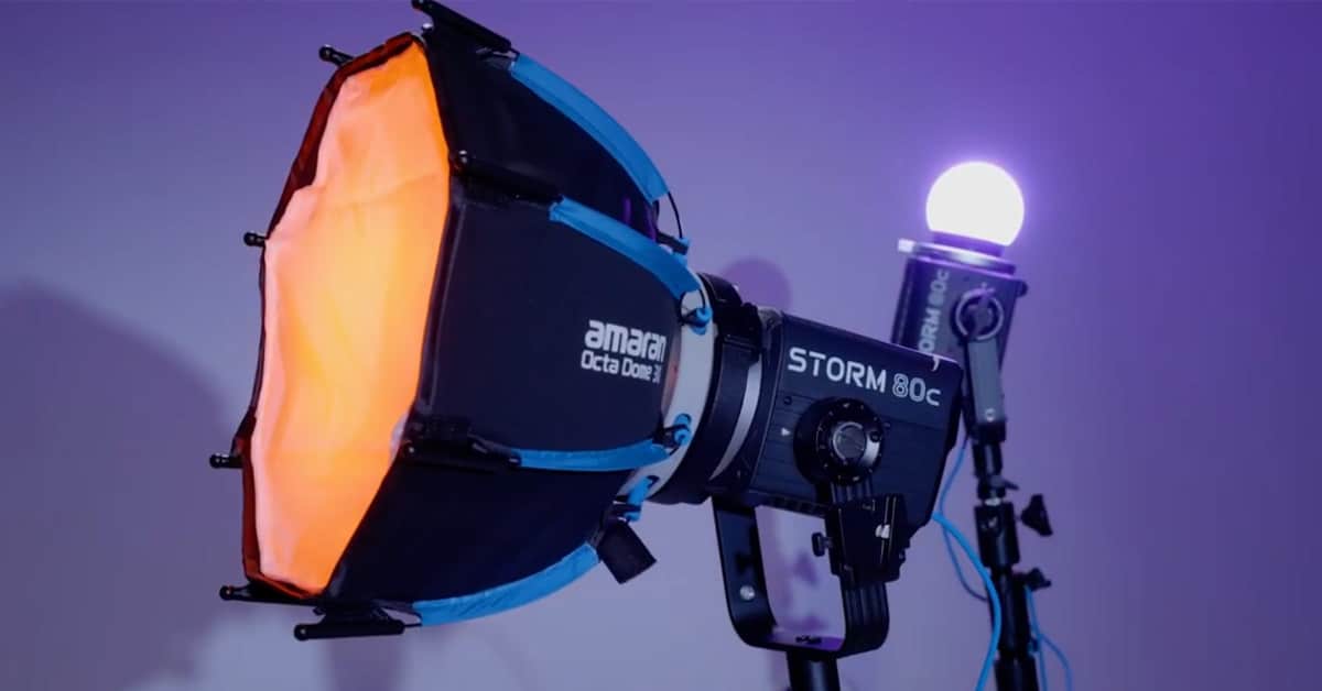 Studio lighting rig: Amaran Storm 80C LED with orange interior softbox on a stand.